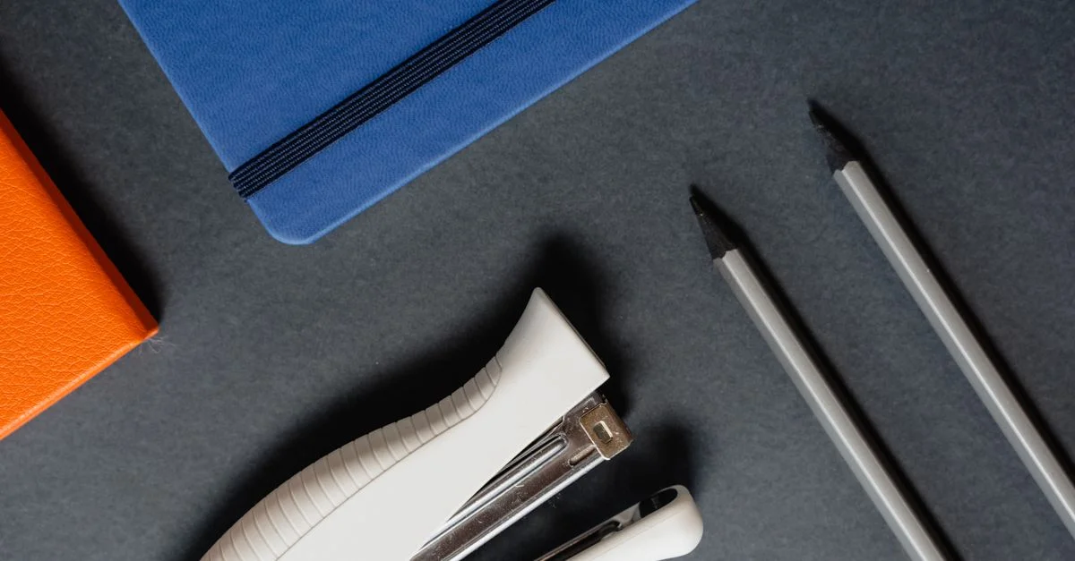 Une mise en scène élégante d'articles de bureau comprenant des carnet, des stylos et une agrafeuse sur un fond sombre.